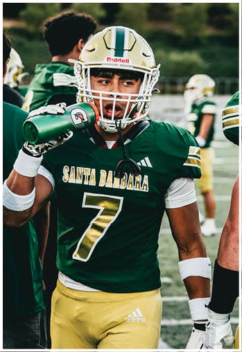 A person wearing a green football jersey with “Santa Barbara" and the number 7 on it and yellow Adidas pants is standing on a field. Description generated by AI