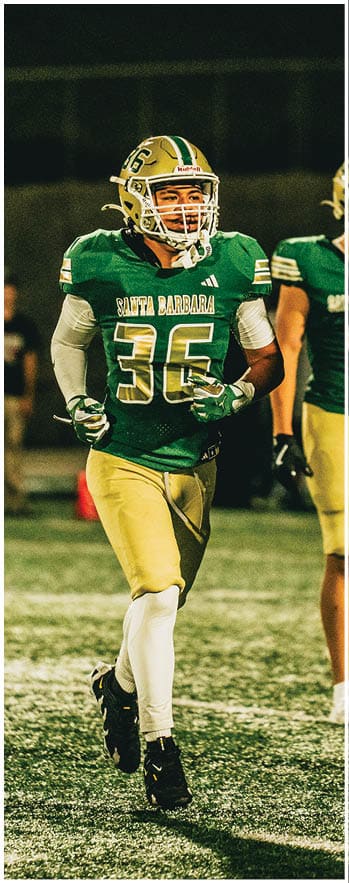 A person wearing a green and gold football uniform with the number 36 and the words Santa Barbara is running on a football field at night. Description generated by AI