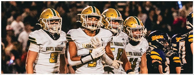 A group of people wearing football uniforms from two different teams stand closely together on a field during a game. Description generated by AI