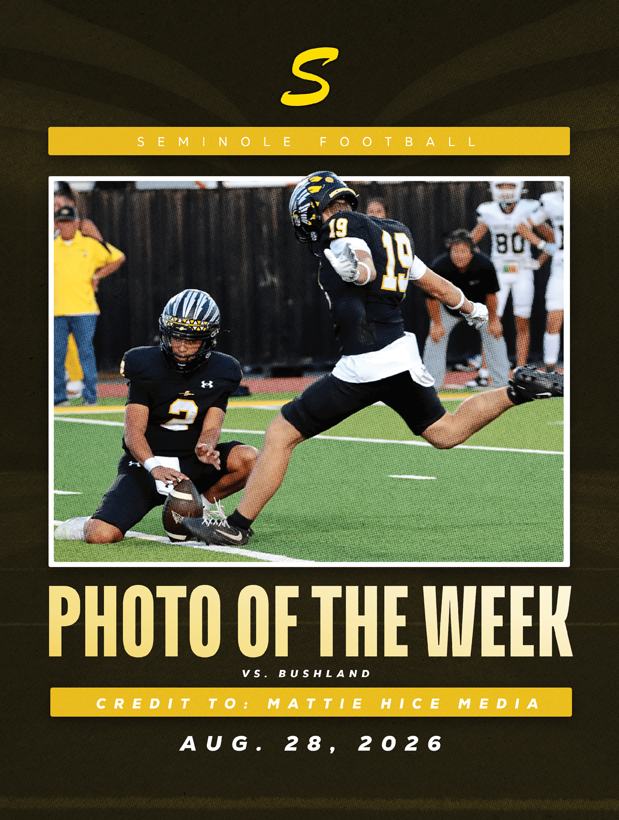Two football players in black uniforms are on a field with one holding the ball for the other to kick during a game. Description generated by AI