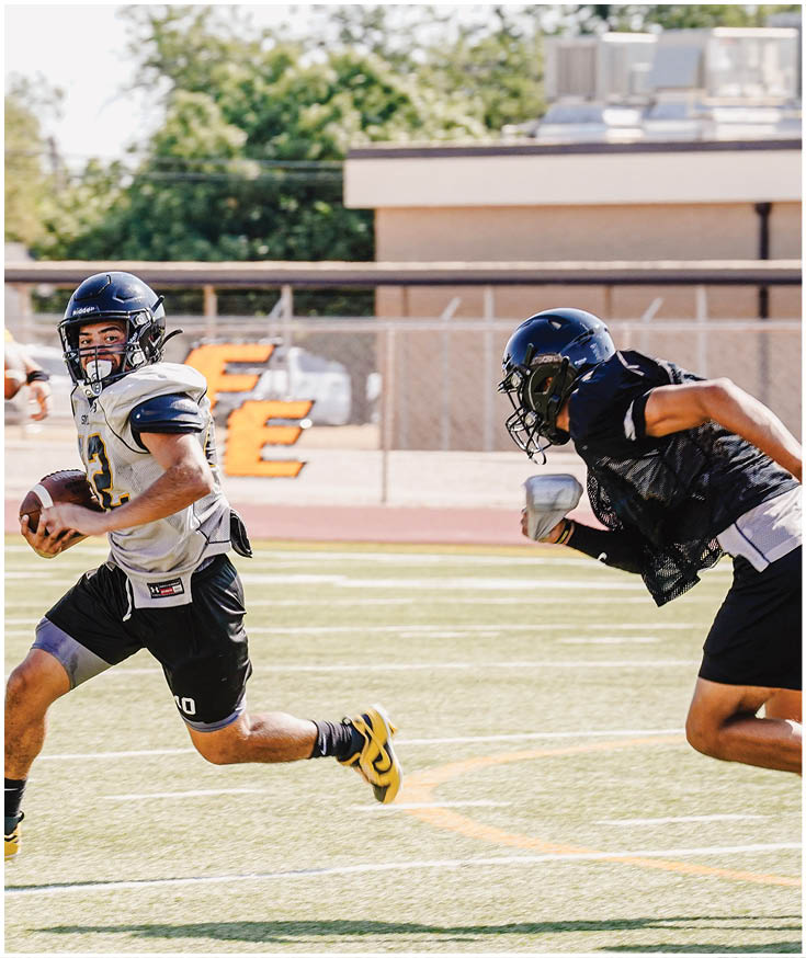Three football players in blue and white uniforms running on a field. Description generated by AI