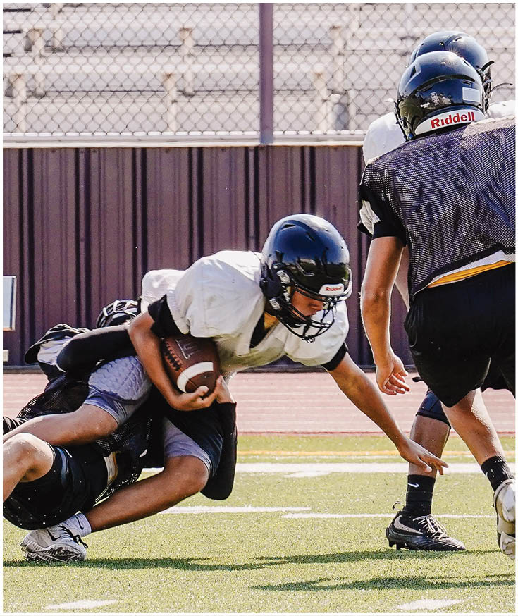 Two people wearing red Gainesville football uniforms stand on grass with their hands clasped in front of them while two others stand in the background near a fence. Description generated by AI