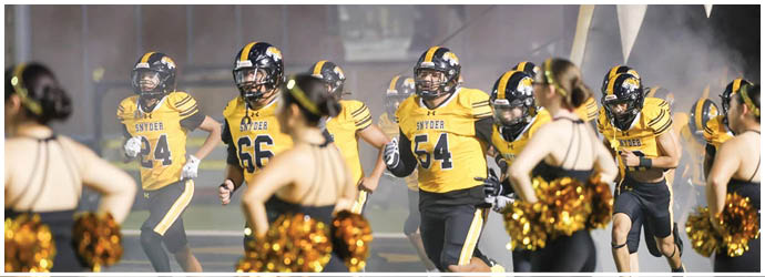 People in yellow and black football uniforms run onto a field while cheerleaders with pom-poms stand in the foreground. Description generated by AI