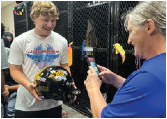 Two people are smiling and interacting in front of black metal lockers decorated with colorful star and circle cutouts. Description generated by AI