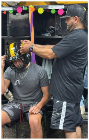 An adult wearing a dark shirt and a smartwatch is reaching towards a decorated black locker with colorful round stickers and hanging orange and purple ribbons. Description generated by AI