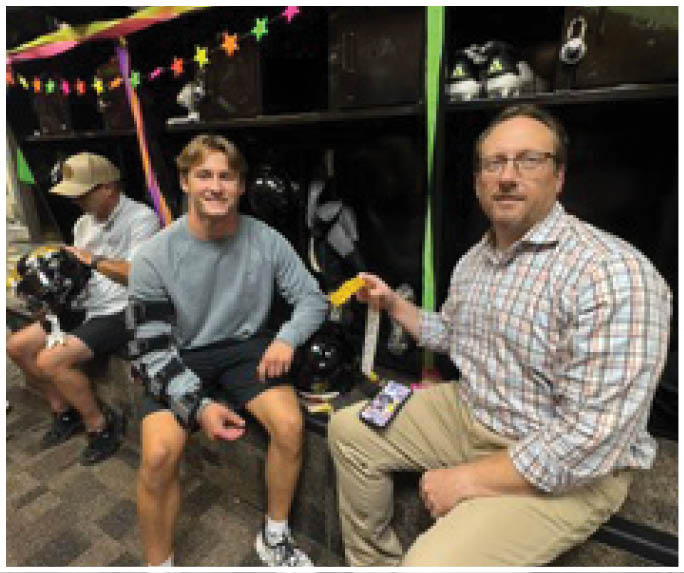 Two adults sitting and smiling in a room decorated with colorful star-shaped garlands and streamers, with shelves holding bags and shoes in the background. Description generated by AI