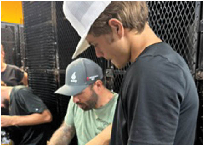Three adults wearing casual clothing and hats are sitting closely together, focused on an activity involving their hands. Description generated by AI