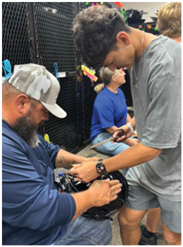 Two adults are closely interacting with a small animal, with one person holding the animal and the other gently touching it, in an indoor setting with a black mesh background. Description generated by AI