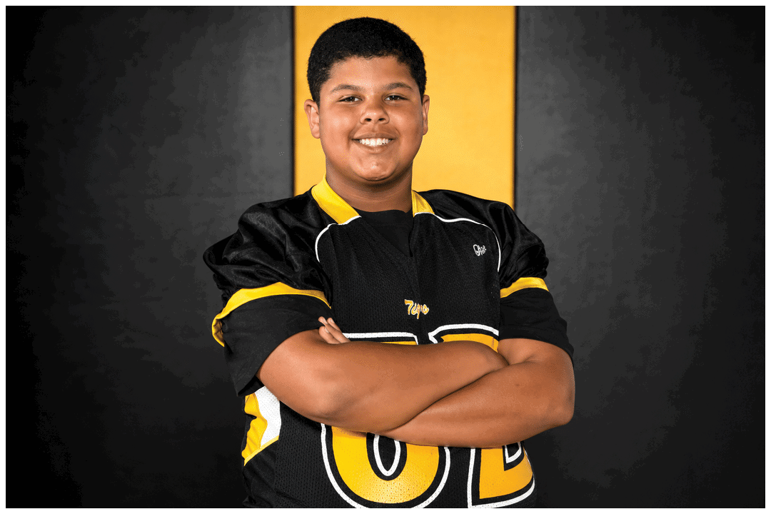 Person wearing a black and yellow sports jersey with arms crossed against a black background. Description generated by AI