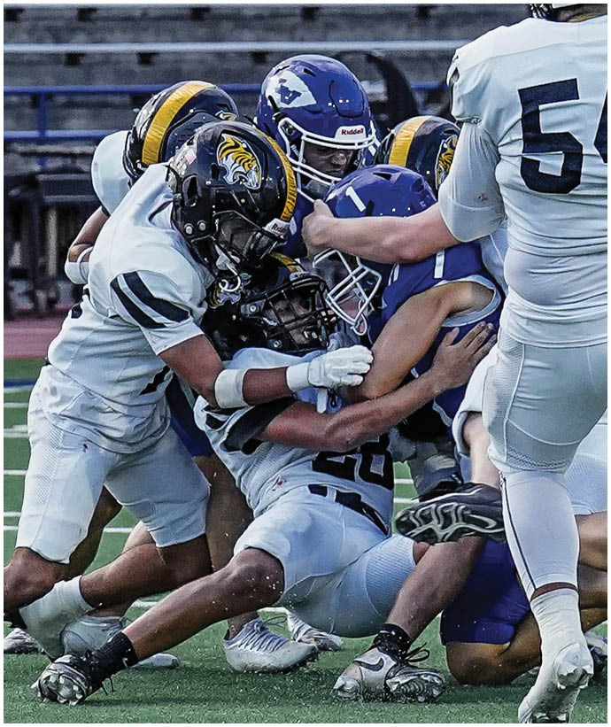 Two people in football uniforms are engaged in a blocking action on a football field during a game. Description generated by AI