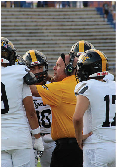 Two people wearing yellow and black football uniforms with helmets stand on a field, one with a wrapped wrist. Description generated by AI