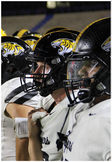 Two people wearing yellow and black football uniforms with helmets stand on a field, one with a wrapped wrist. Description generated by AI