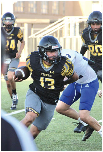 A coach wearing a headset is talking to two football players in yellow and black uniforms on a field. Description generated by AI