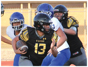 People in yellow and black football uniforms are on a field with one player in a white and purple uniform facing them. Description generated by AI