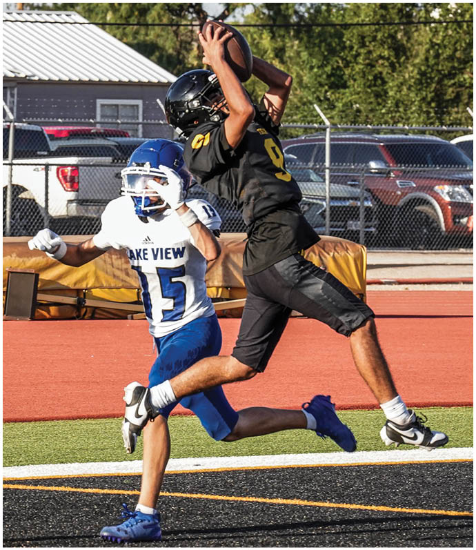 Two people in yellow and black football uniforms are playing against opponents in white and purple uniforms on a football field with spectators in the background. Description generated by AI