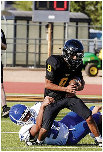 A coach wearing a headset is talking to two football players in yellow and black uniforms on a field. Description generated by AI