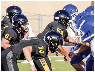 People in yellow and black football uniforms are on a field with one player in a white and purple uniform facing them. Description generated by AI