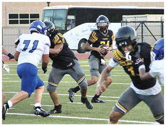 People in yellow and black football uniforms run onto a field holding American and Texas flags with a large inflatable tiger head in the background. Description generated by AI