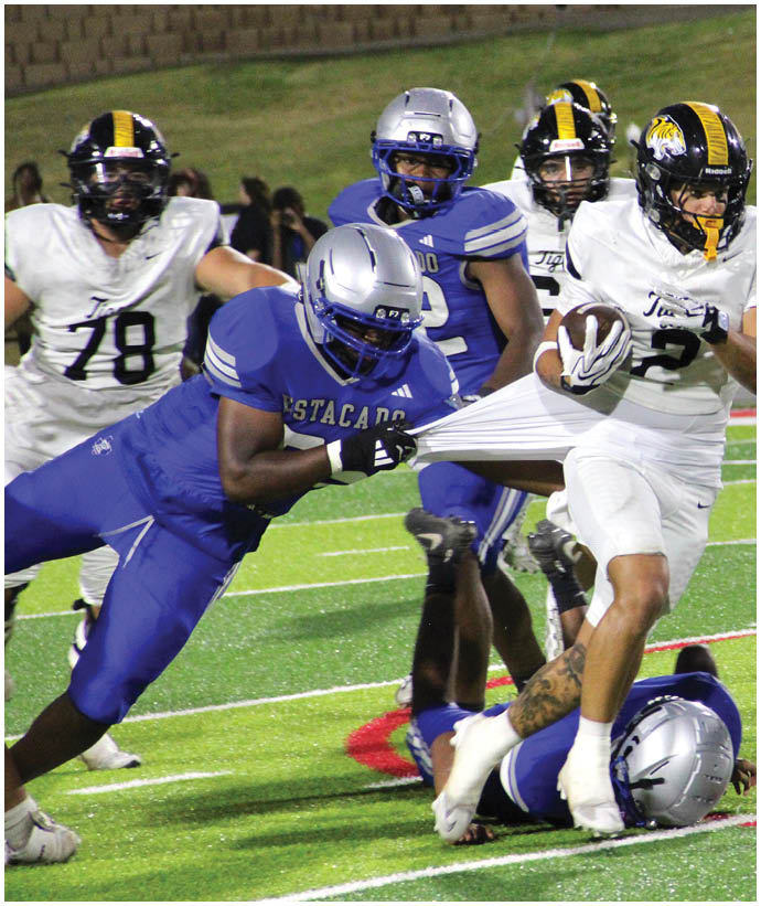 Two people in blue football uniforms with silver helmets are actively engaged in a play on a football field, with one person grabbing the shirt of an opponent. Description generated by AI
