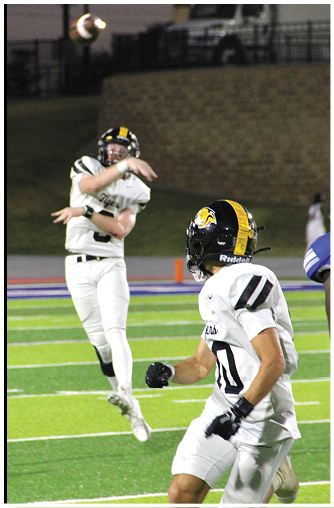 Two people wearing football helmets and uniforms are engaged in a play on a field, with one person preparing to throw a football. Description generated by AI