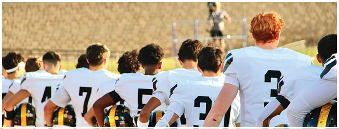A group of people wearing white sports jerseys with numbers on the back are standing side by side with their arms around each other. Description generated by AI