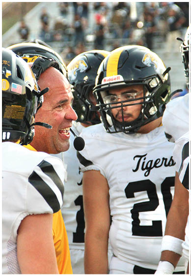 A group of people in football uniforms and helmets are gathered closely, with one person speaking into a headset microphone. Description generated by AI