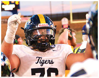 A person wearing a football helmet and a white jersey with “Tigers" and the number 70 is raising their arms in celebration on a football field. Description generated by AI