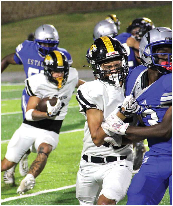 Two people in white and black football uniforms are running on a field while two people in blue and silver uniforms pursue them. Description generated by AI
