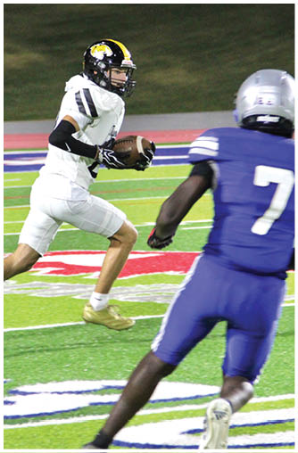 A person in a white football uniform is running with the ball while another person in a blue uniform approaches on a football field. Description generated by AI
