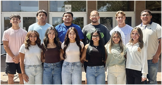 A group of ten adults standing in two rows on steps outside a building labeled P. Worsham Auditorium, smiling and casually dressed in jeans and shirts. Description generated by AI
