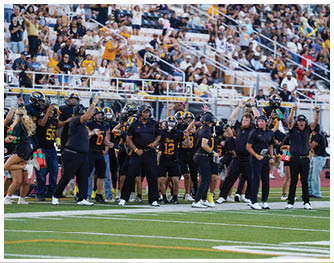 A group of people in black sports uniforms and coaches are standing on a football field with a crowd of spectators in the background. Description generated by AI