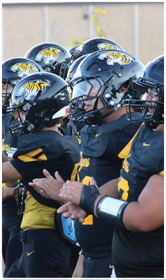 A group of people wearing black and yellow football uniforms and helmets are standing in a line, some clapping. Description generated by AI