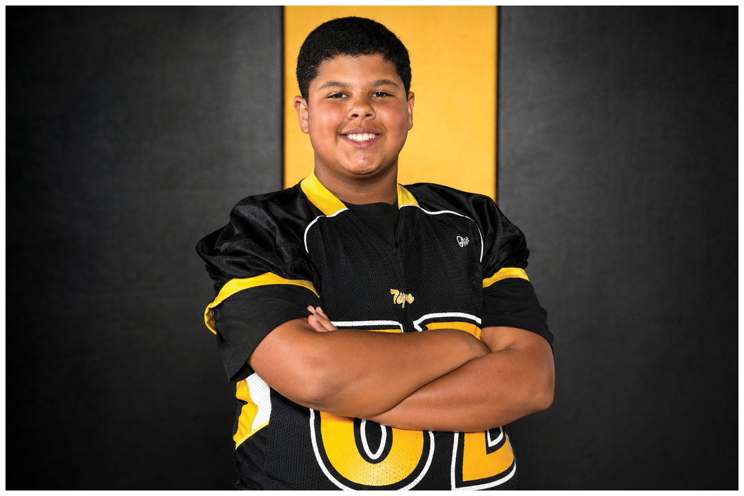 Person wearing a black and yellow sports jersey with arms crossed against a black background. Description generated by AI