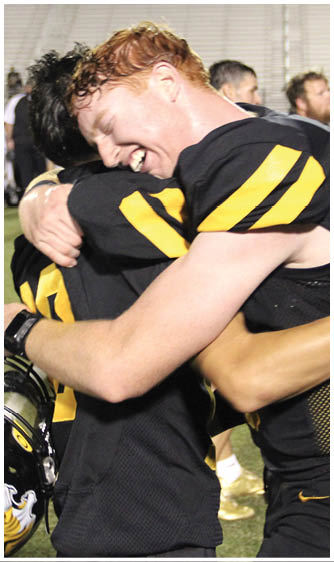 Two people wearing black and yellow sports uniforms are embracing each other on a field, with one person smiling broadly. Description generated by AI