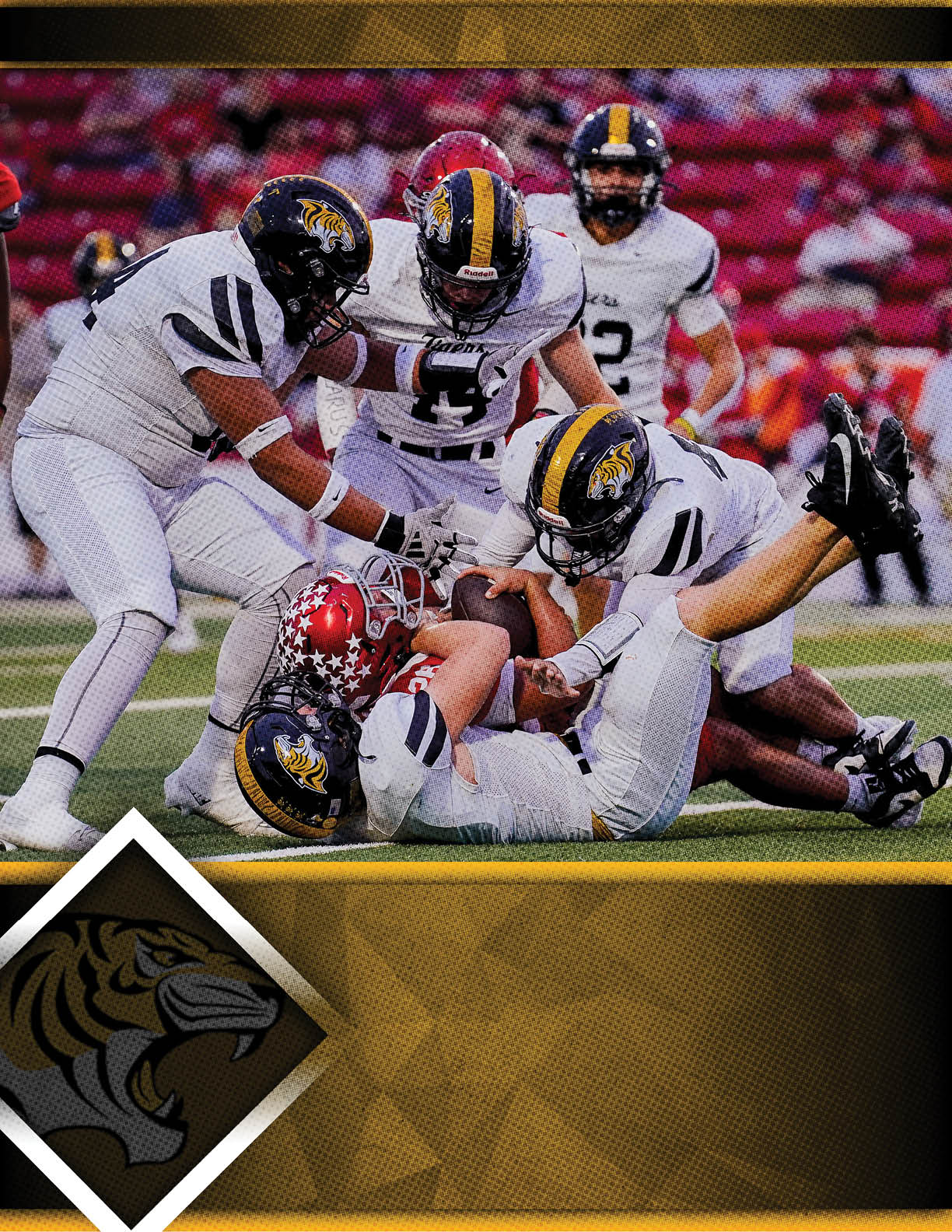 Several football players in white uniforms with black and yellow helmets are tackling a player in a red uniform on a green field with a blurred crowd in the background. Description generated by AI