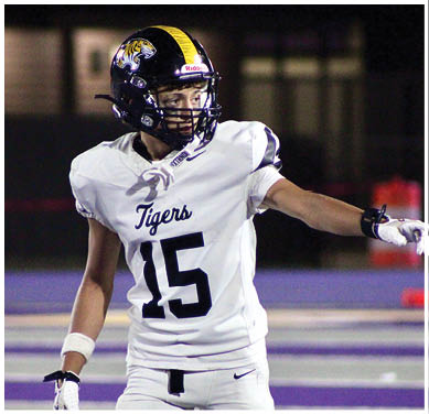 A person wearing a white football uniform with the number 15 and a black helmet with a tiger logo is pointing to the side on a football field. Description generated by AI