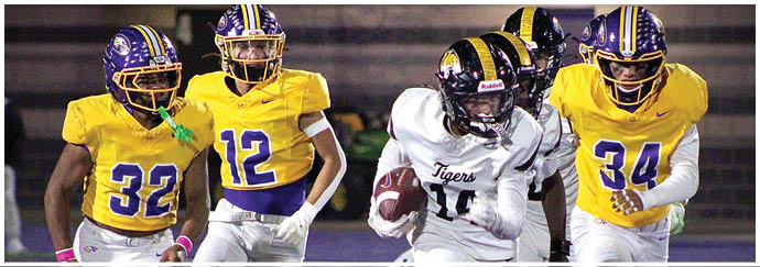 A person in a white football uniform is running with the ball while three people in yellow and purple uniforms chase them on a football field. Description generated by AI