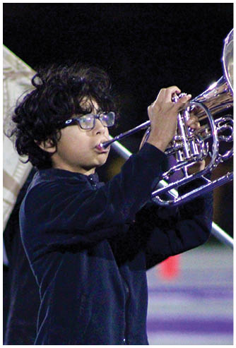 Person with curly hair and glasses playing a brass instrument outdoors at night. Description generated by AI