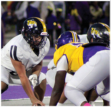 Two people in football uniforms and helmets are crouched facing each other on a field, appearing ready for a play. Description generated by AI