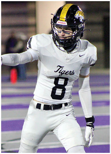 A person wearing a white football uniform with the number 8 and a black and yellow helmet is pointing while standing on a field. Description generated by AI