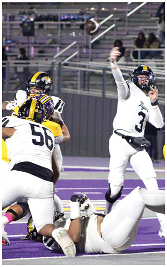 Two people in football uniforms are engaged in a play on a field with purple and white markings, with one person raising an arm and another person on the ground. Description generated by AI