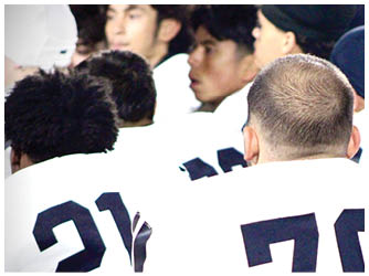 People wearing sports uniforms with numbers on their backs are gathered closely together, likely during a team event or game. Description generated by AI