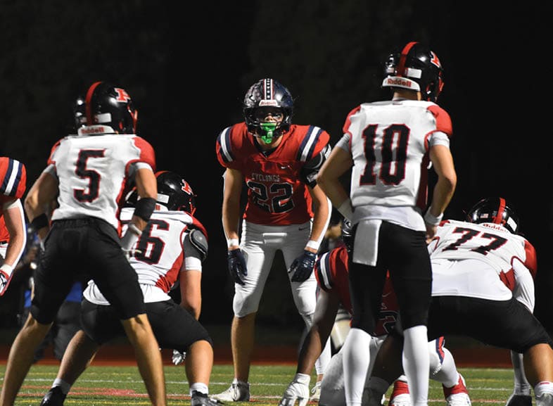 Four people wearing black football uniforms with “VISTA" on the front are standing together in a stadium with a crowd in the background, two of them holding helmets raised above their heads. Description generated by AI