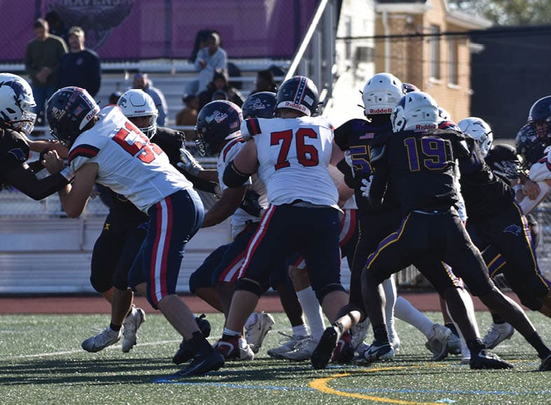 Four people wearing black football uniforms with “VISTA" on the front are standing together in a stadium with a crowd in the background, two of them holding helmets raised above their heads. Description generated by AI