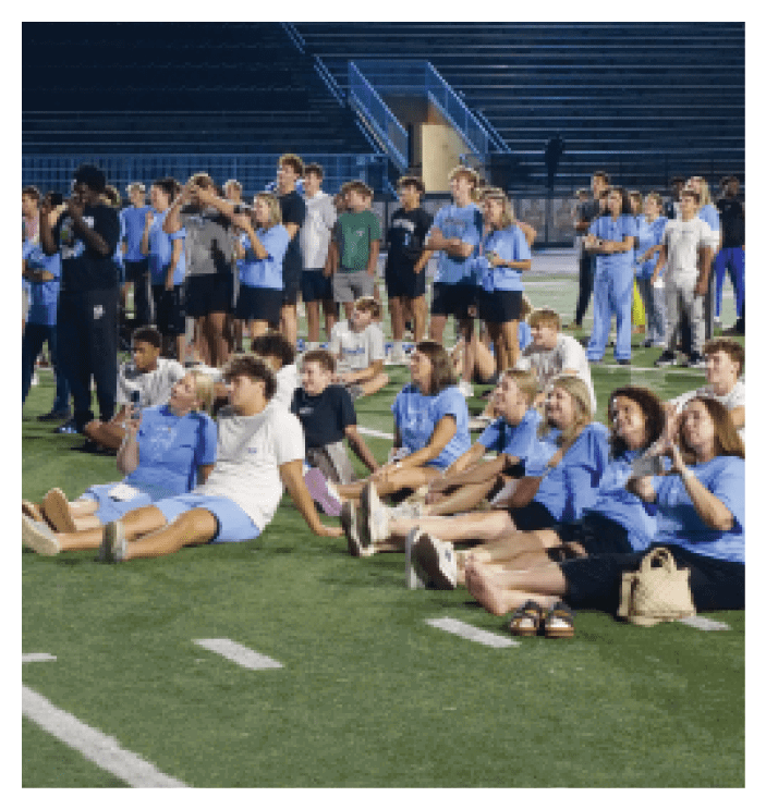 A group of people are sitting on a field, some of them holding drinks. AI generated content