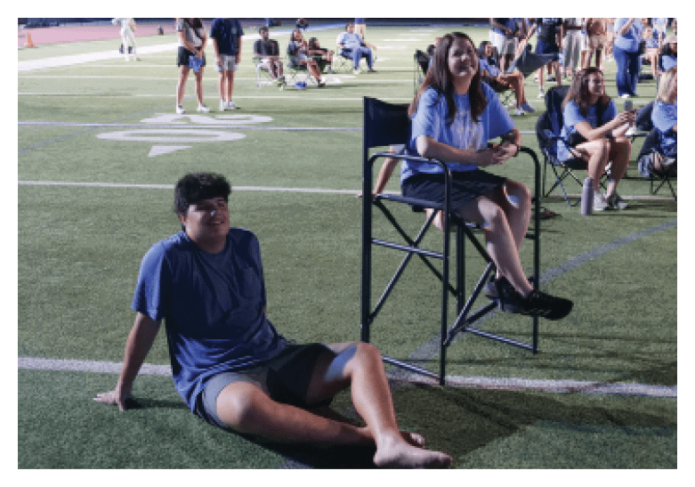 Two people are sitting on chairs on a field. One person is sitting on a stool, while the other is sitting on a chair. They are both smiling and appear to be enjoying their time together. AI generated content