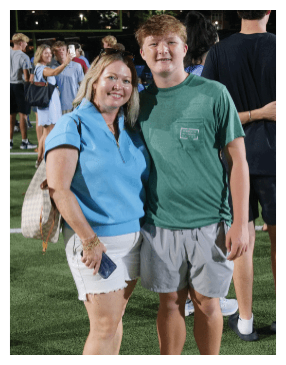 A woman and a boy are standing on a field, posing for a picture. The woman is wearing a blue shirt and holding a purse. The boy is wearing a green shirt. AI generated content