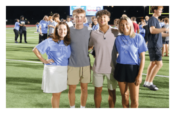 Four people are standing on a field, posing for a picture. They are all wearing blue shirts. AI generated content