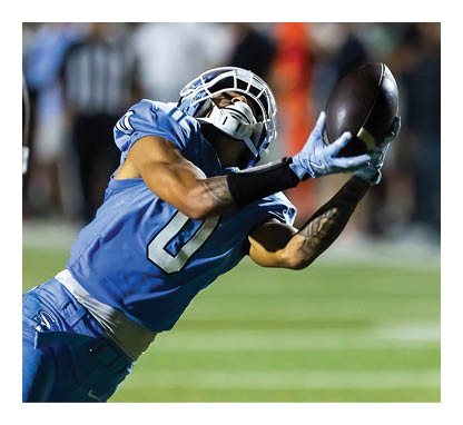 A football player wearing a blue jersey is trying to catch a football. AI generated content