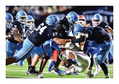 A group of football players in blue uniforms are playing a game. One player is tackling another player who is on the ground. AI generated content